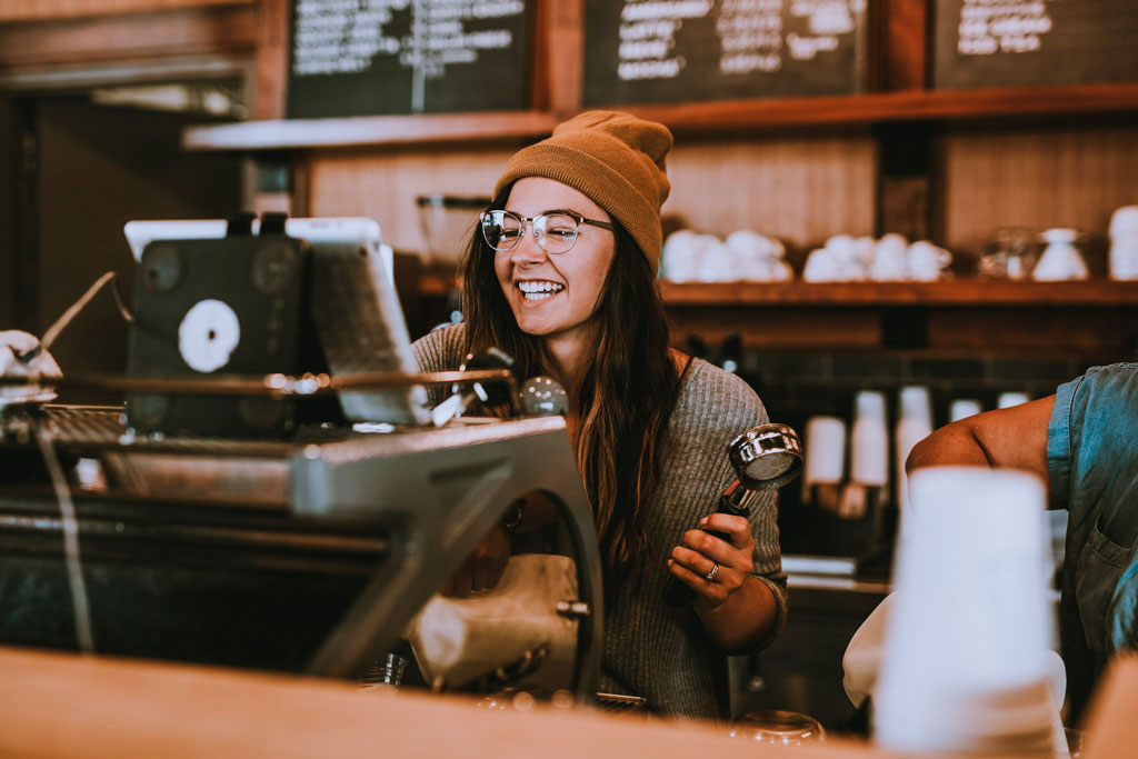 woman quickly checking out customer with help of strong it infrastructure while also making coffee behind cafe counter