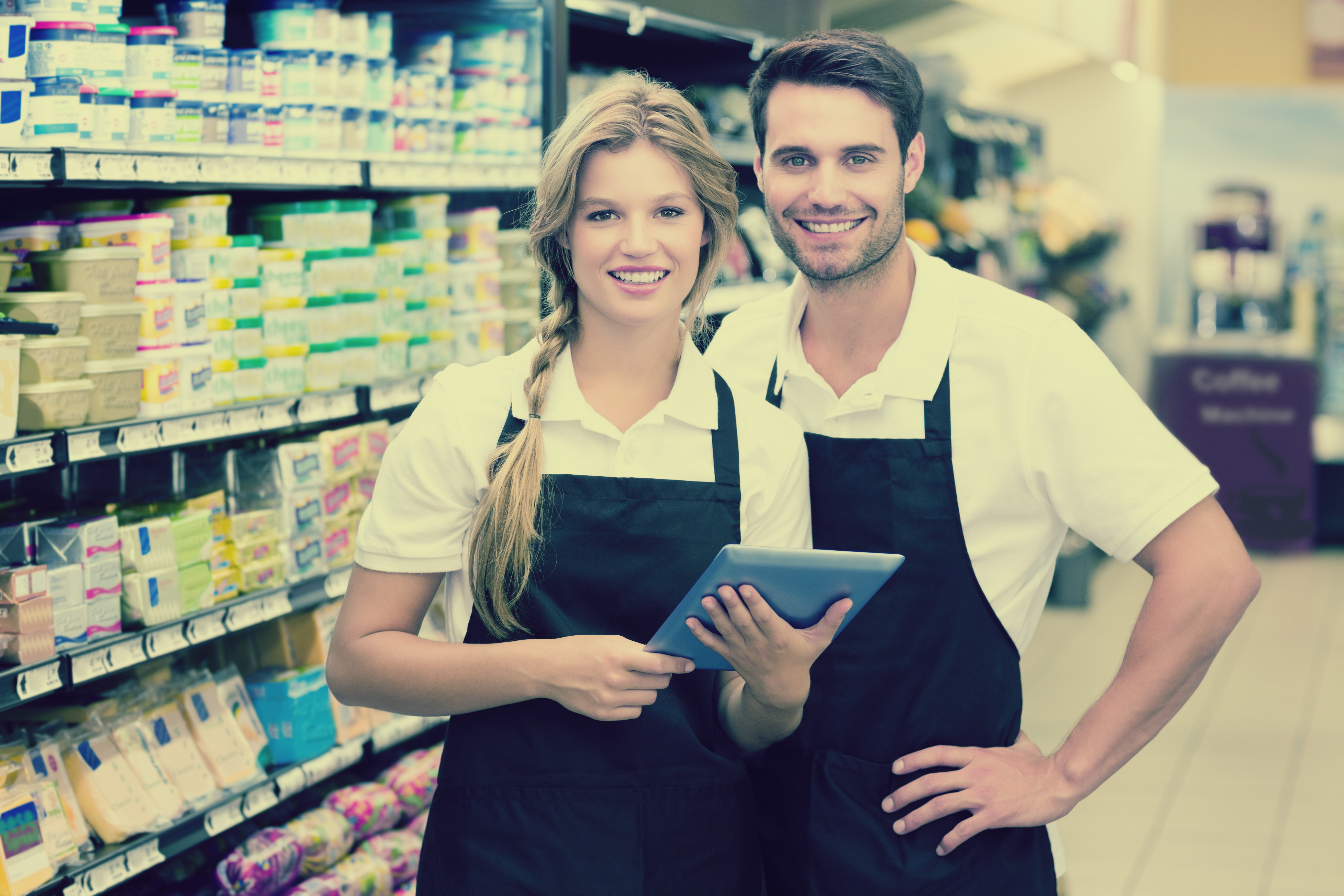 Learning Management Systems and Seasonal Employees | Worldlink Integration Group | Smiling male and female employees using a tablet for training near stocking shelves