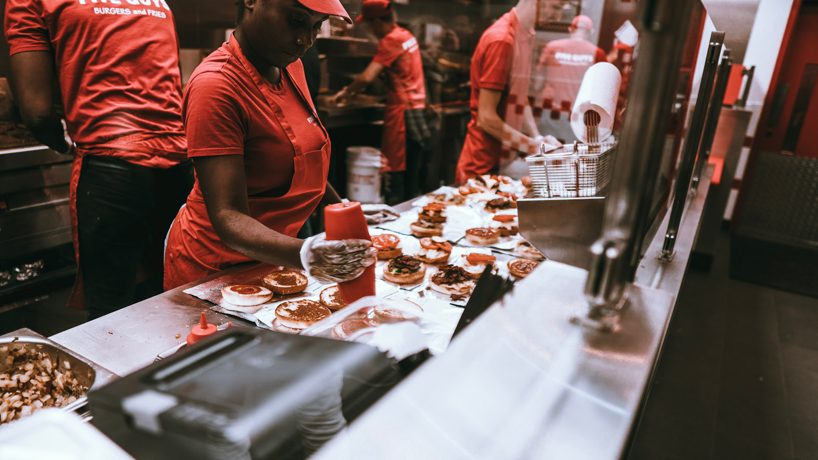five guys staff member putting ketchup on burgers