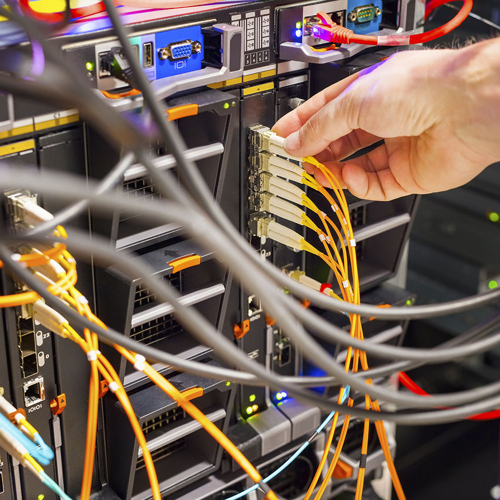 Closeup of IT technician's hand plugging fiber channel cable into switch in datacenter